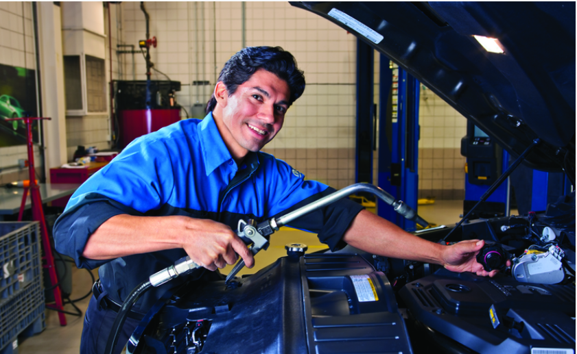 Mechanic performing vehicle maintenance under the hood in an automotive service center