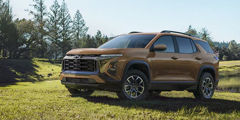 Bronze Chevrolet Equinox SUV parked on a grassy field surrounded by trees.