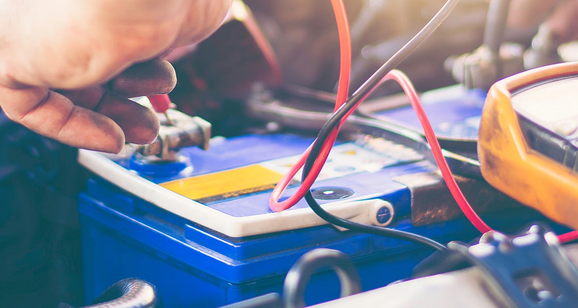 Mechanic testing a car battery with a multimeter